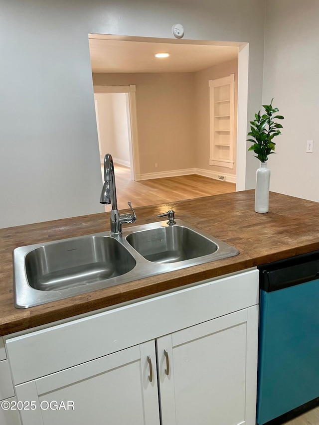 kitchen with white cabinets, dark countertops, dishwashing machine, light wood-style floors, and a sink