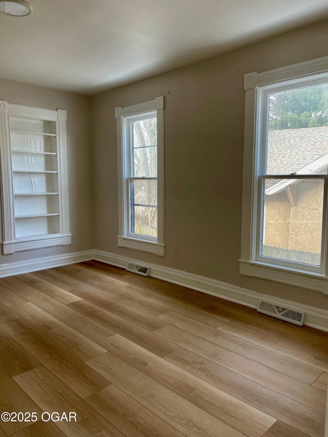 unfurnished room featuring light wood finished floors, visible vents, and baseboards