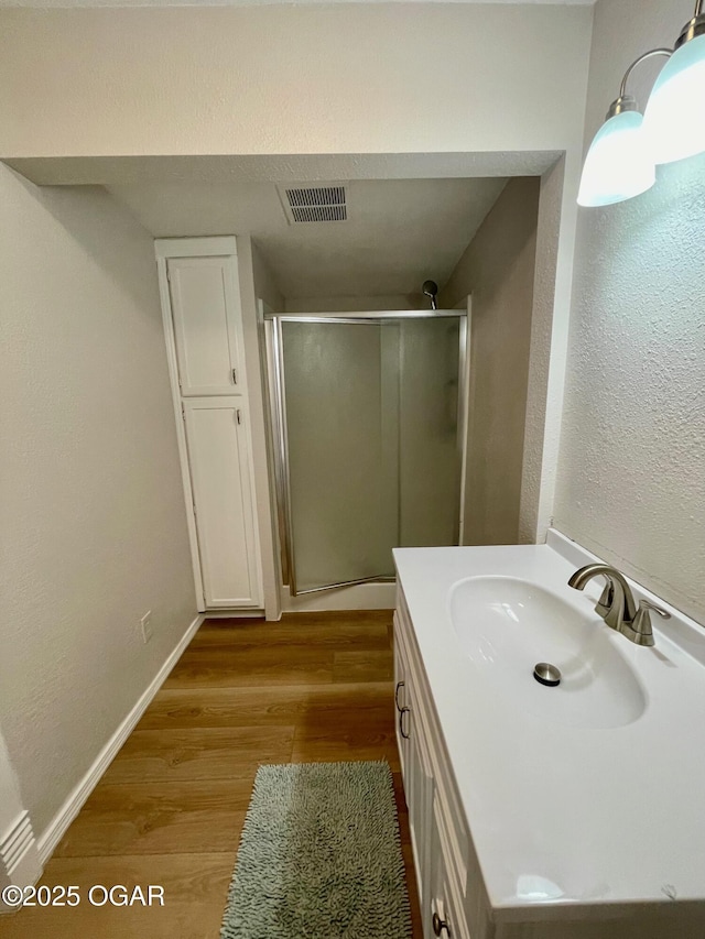 bathroom featuring wood finished floors, visible vents, baseboards, vanity, and a shower stall