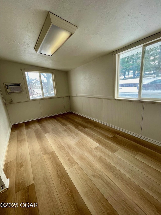 unfurnished room featuring a wall unit AC, light wood-type flooring, a textured ceiling, and wainscoting