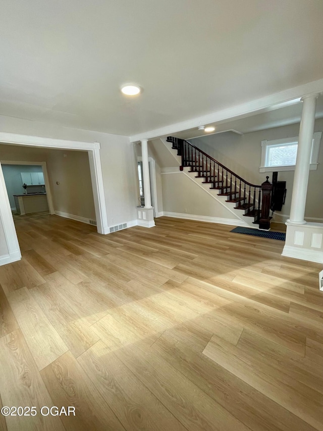 spare room featuring light wood finished floors, stairway, and decorative columns