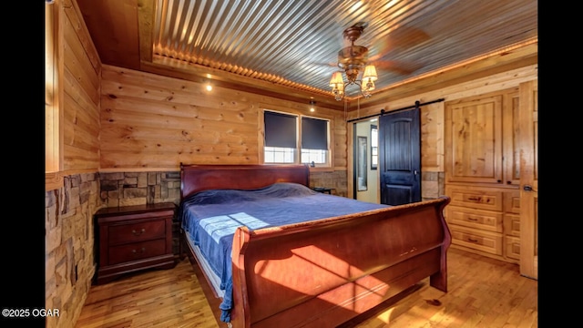 bedroom with wooden ceiling, a barn door, and light hardwood / wood-style floors