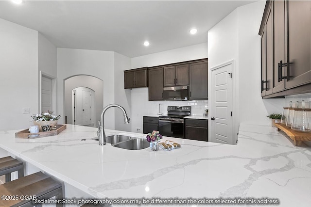 kitchen featuring a breakfast bar, light stone counters, electric stove, and sink