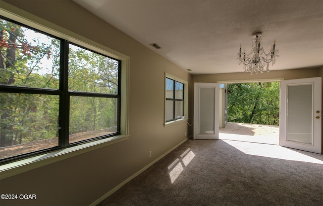 carpeted spare room with a wealth of natural light and a chandelier