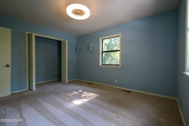 unfurnished bedroom featuring a closet, a textured ceiling, and light colored carpet