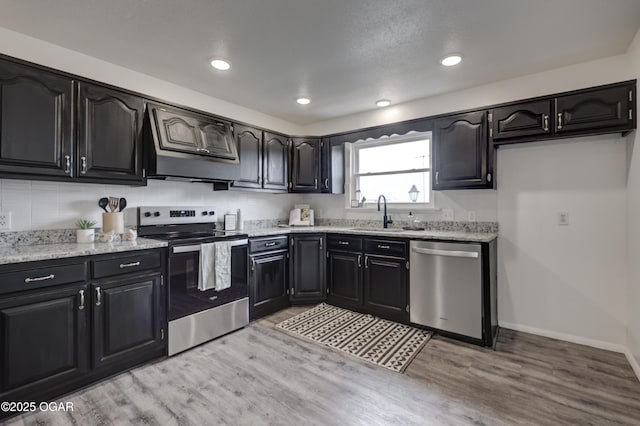 kitchen with sink, stainless steel appliances, custom range hood, and light wood-type flooring