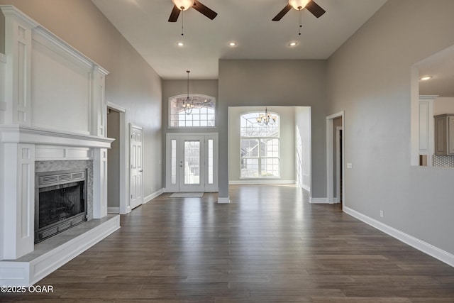 unfurnished living room with dark hardwood / wood-style flooring, ceiling fan with notable chandelier, and a high ceiling