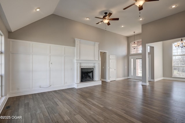 unfurnished living room with high vaulted ceiling, dark wood-type flooring, and ceiling fan with notable chandelier