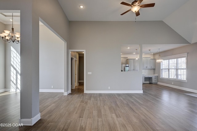 unfurnished living room featuring lofted ceiling, ceiling fan with notable chandelier, and hardwood / wood-style flooring