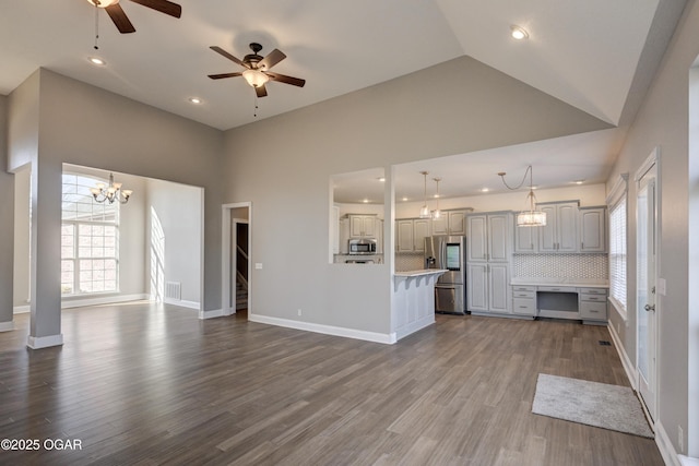 unfurnished living room with ceiling fan with notable chandelier, hardwood / wood-style floors, and high vaulted ceiling