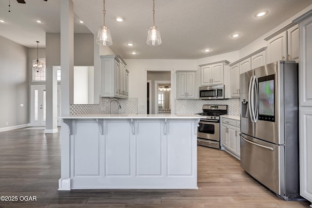 kitchen with light wood-type flooring, appliances with stainless steel finishes, ceiling fan with notable chandelier, and kitchen peninsula