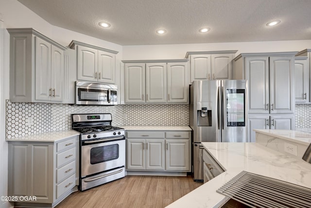 kitchen featuring light wood-type flooring, stainless steel appliances, tasteful backsplash, and light stone countertops