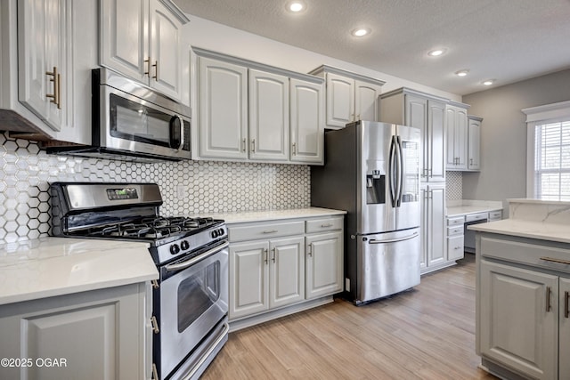 kitchen featuring a textured ceiling, stainless steel appliances, light hardwood / wood-style floors, and gray cabinets