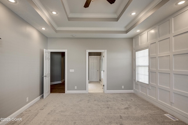 unfurnished bedroom featuring ceiling fan, crown molding, light colored carpet, and a raised ceiling