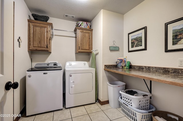 clothes washing area featuring a textured ceiling, cabinets, washing machine and clothes dryer, and light tile patterned floors