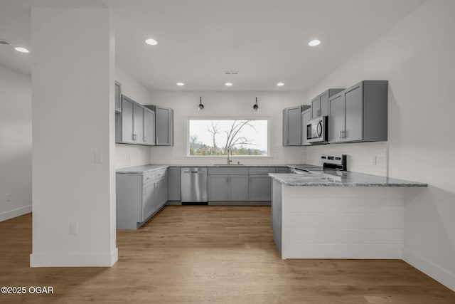 kitchen featuring sink, gray cabinetry, light stone counters, appliances with stainless steel finishes, and kitchen peninsula