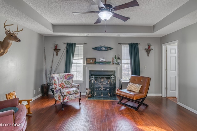 sitting room with ceiling fan, dark wood-type flooring, a textured ceiling, and a tray ceiling