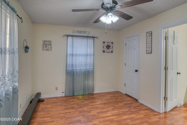 empty room with a textured ceiling, ceiling fan, and light hardwood / wood-style floors