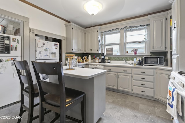 kitchen with decorative backsplash, white appliances, white cabinets, a breakfast bar, and sink