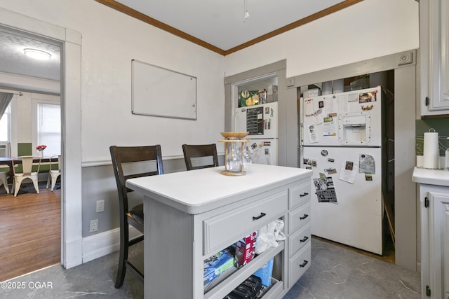 kitchen featuring a kitchen island, crown molding, white cabinetry, white refrigerator with ice dispenser, and a kitchen breakfast bar