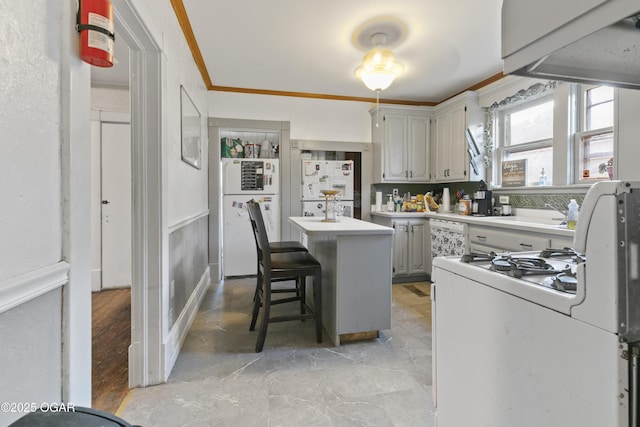 kitchen with white appliances, ornamental molding, a breakfast bar area, and a kitchen island