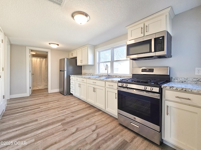 kitchen with light stone countertops, a textured ceiling, appliances with stainless steel finishes, sink, and light hardwood / wood-style flooring