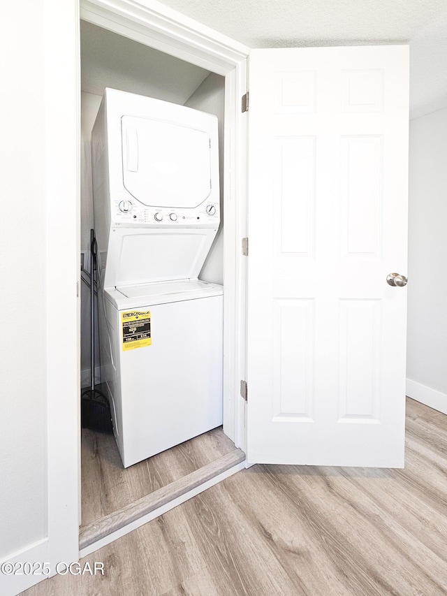 laundry area with light hardwood / wood-style floors and stacked washing maching and dryer