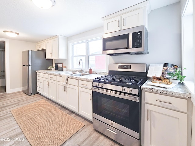 kitchen with light wood-type flooring, sink, appliances with stainless steel finishes, and white cabinets