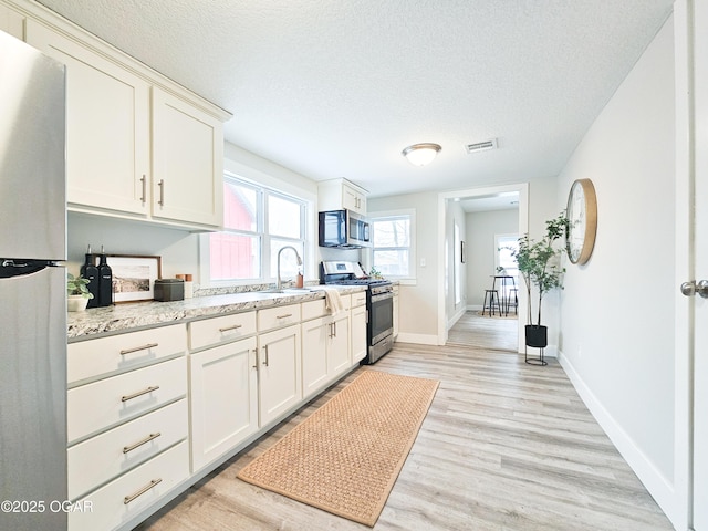 kitchen featuring stainless steel appliances, light hardwood / wood-style flooring, light stone countertops, sink, and a textured ceiling