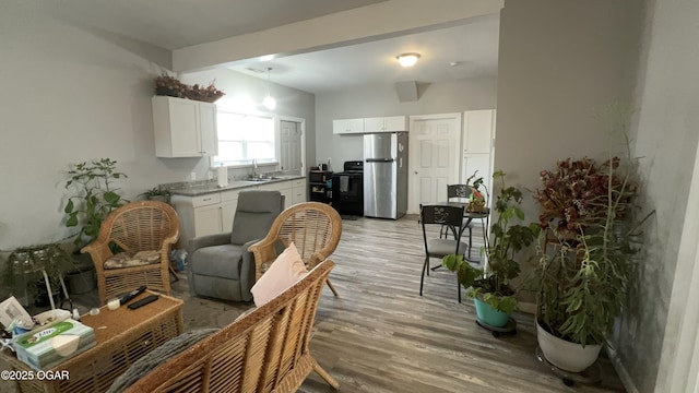 kitchen featuring white cabinetry, stainless steel fridge, light wood-type flooring, stove, and sink