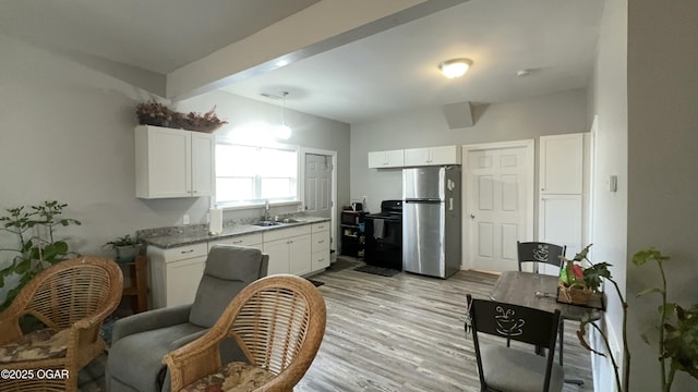 kitchen featuring white cabinetry, black electric range, stainless steel refrigerator, light stone counters, and sink