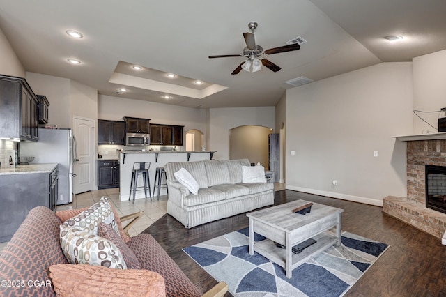 living room with ceiling fan, dark hardwood / wood-style flooring, a raised ceiling, and a fireplace