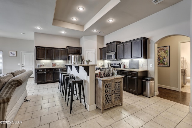 kitchen with light tile patterned floors, a kitchen bar, appliances with stainless steel finishes, and an island with sink