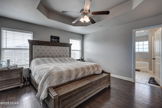 bedroom featuring ceiling fan, dark hardwood / wood-style floors, a tray ceiling, and ensuite bath