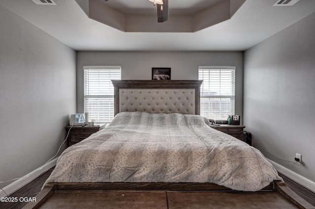 bedroom featuring ceiling fan, dark hardwood / wood-style flooring, and a raised ceiling