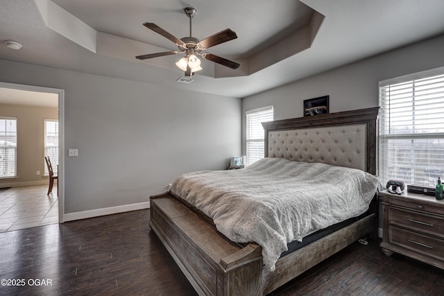 bedroom with ceiling fan, dark hardwood / wood-style floors, and a tray ceiling