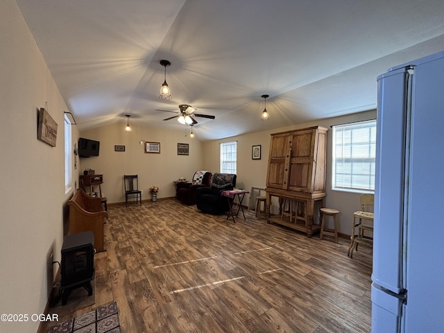 living room featuring ceiling fan, dark wood-type flooring, a wood stove, and vaulted ceiling