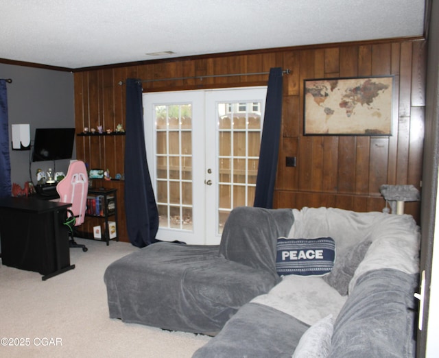 carpeted living room with french doors, crown molding, and wood walls