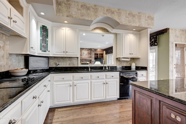 kitchen featuring sink, light wood-type flooring, white cabinets, dark stone counters, and black appliances