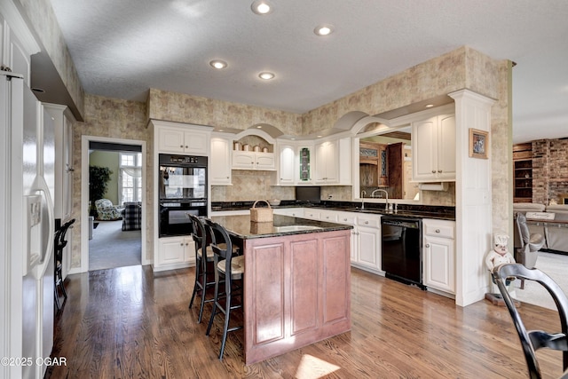 kitchen featuring hardwood / wood-style flooring, a center island, white cabinets, and black appliances