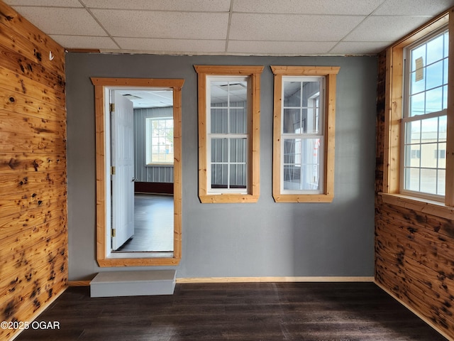 spare room featuring a drop ceiling, dark hardwood / wood-style floors, and wood walls