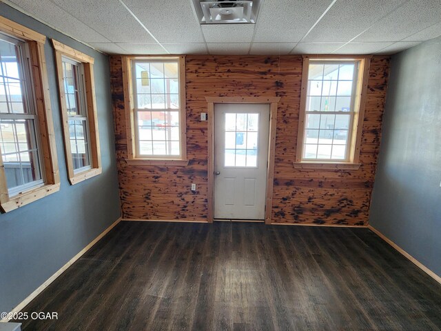 interior space with dark wood-type flooring, a paneled ceiling, and wood walls