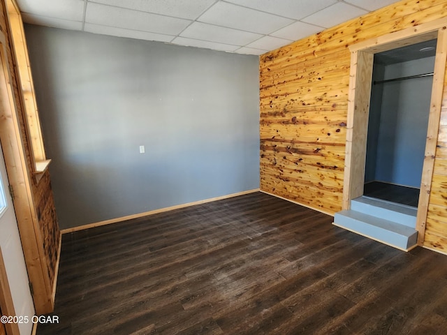 unfurnished room featuring dark wood-type flooring, a drop ceiling, and wood walls