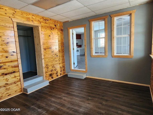 unfurnished room with a paneled ceiling, dark wood-type flooring, and wood walls