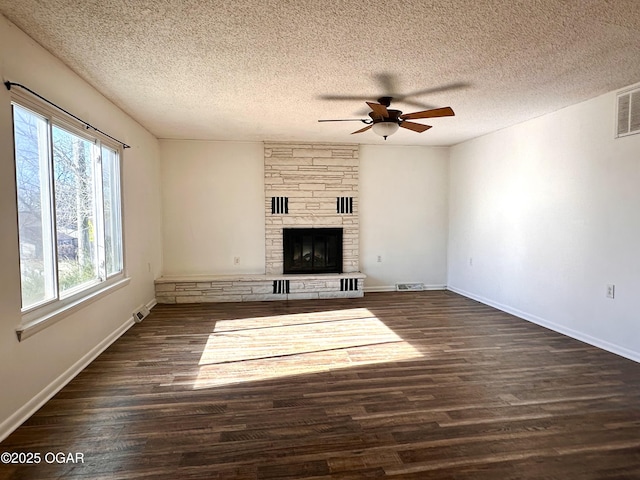 unfurnished living room featuring ceiling fan, a textured ceiling, dark hardwood / wood-style floors, and a stone fireplace