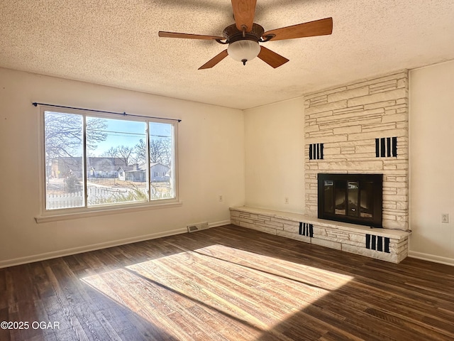 unfurnished living room with ceiling fan, dark wood-type flooring, a stone fireplace, and a textured ceiling