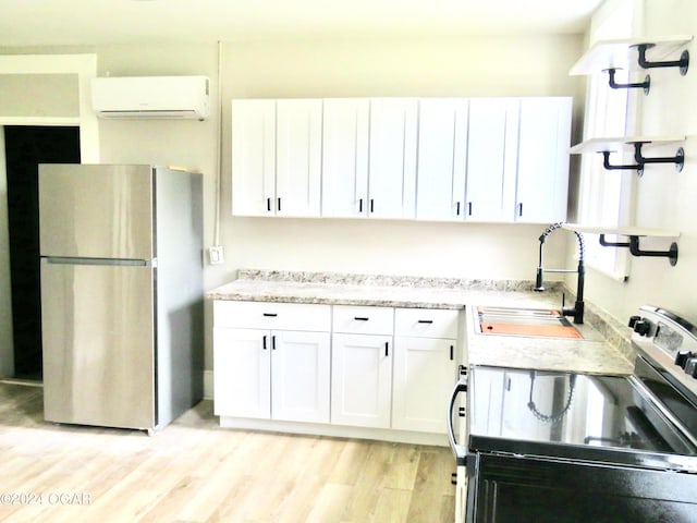 kitchen featuring appliances with stainless steel finishes, white cabinetry, light hardwood / wood-style floors, sink, and a wall unit AC