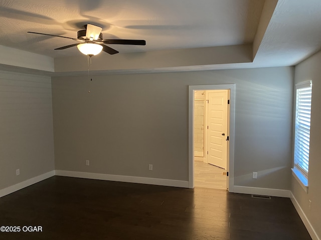 unfurnished room featuring ceiling fan, a tray ceiling, and dark hardwood / wood-style flooring