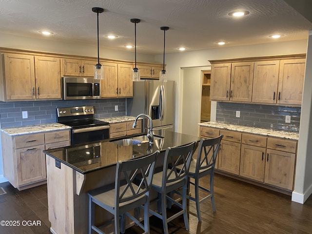 kitchen featuring stainless steel appliances, sink, a kitchen island with sink, and dark stone counters