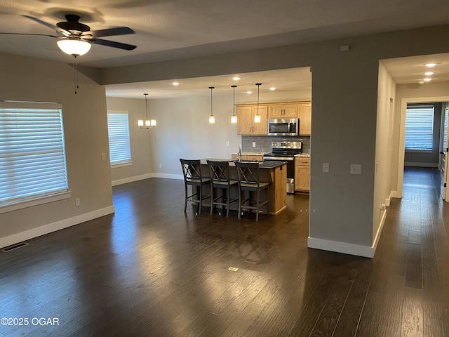 kitchen with an island with sink, a breakfast bar area, backsplash, stainless steel appliances, and light brown cabinets